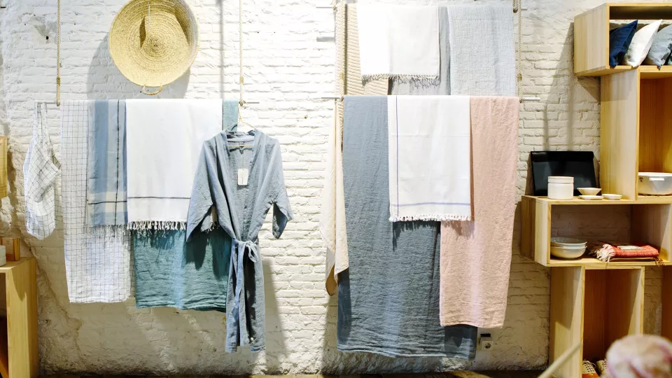 Kläder och handdukar, upphängda vid en vit vägg i en butik. Foto.