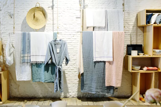 Kläder och handdukar, upphängda vid en vit vägg i en butik. Foto.
