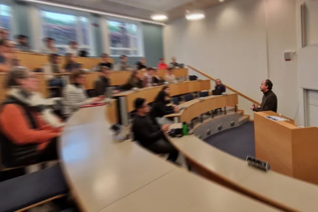 Delvis suddigt fotografi på Markus Lahtinen som talar för människor i en föreläsningssal. 