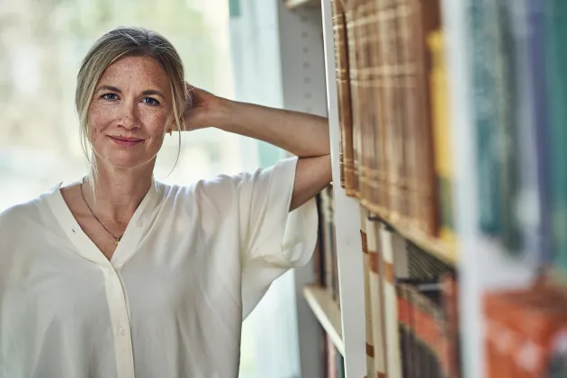 En kvinna i vit skjorta står framför en bokhylla med gamla böcker. Foto.