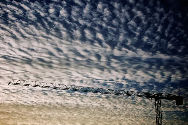 En byggarbetskran mot en himmel med moln. Foto.