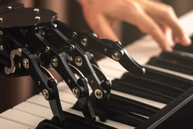 Robothand och människohand som spelar på ett piano, sida vid sida. Foto.