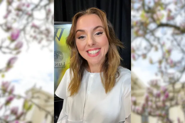 Porträttbild på Erika Hultman som ler mot kameran. Oskarp bild på magnolior i bakgrunden. 