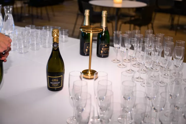 Alkoholfritt bubbel korkas upp och champagneglas är uppradade på bord för firande