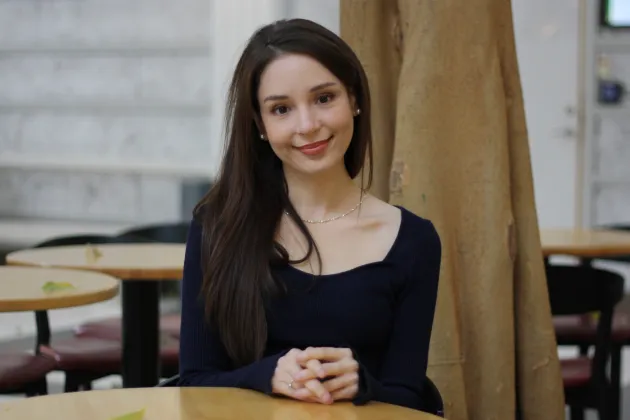 Fotografi av Megan Answers som sitter vid ett runt bord och ler mot kameran. 