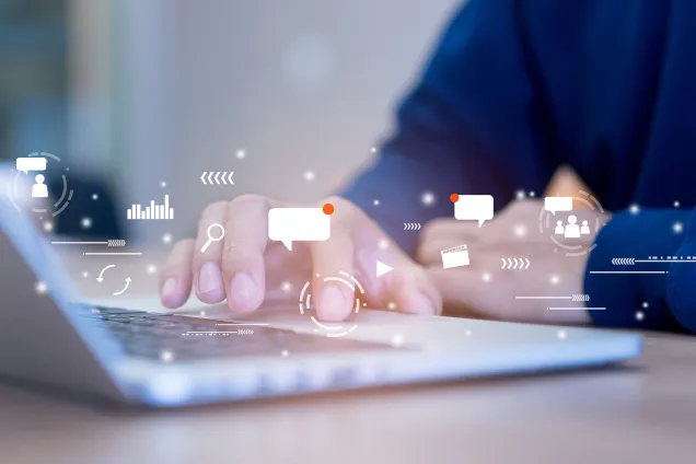 Ett par händer vid en bärbar dator. Över bilden är ett antal ikoner placerade, typ grafer och pratbubblor. Montage av foto och illustration.