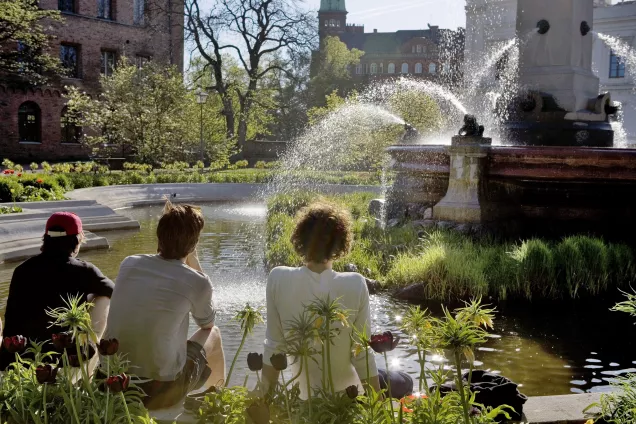 Tre studenter sitter och betraktar universitetsplatsens fontän