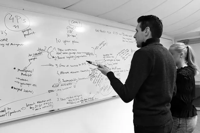 Två personer framför en whiteboard full med text. Foto