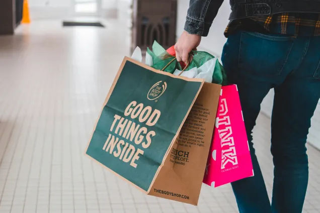 Persons nedre kroppshalva bakifrån, hållandes ett antal shoppingpåsar. Foto.
