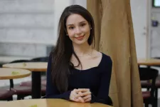 Fotografi av Megan Answers som sitter vid ett runt bord och ler mot kameran. 