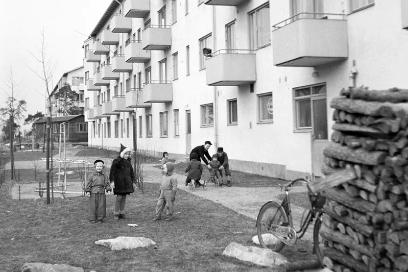 Barn står framför nybyggda flerfamiljshus. Svartvitt foto från 1940-talet.